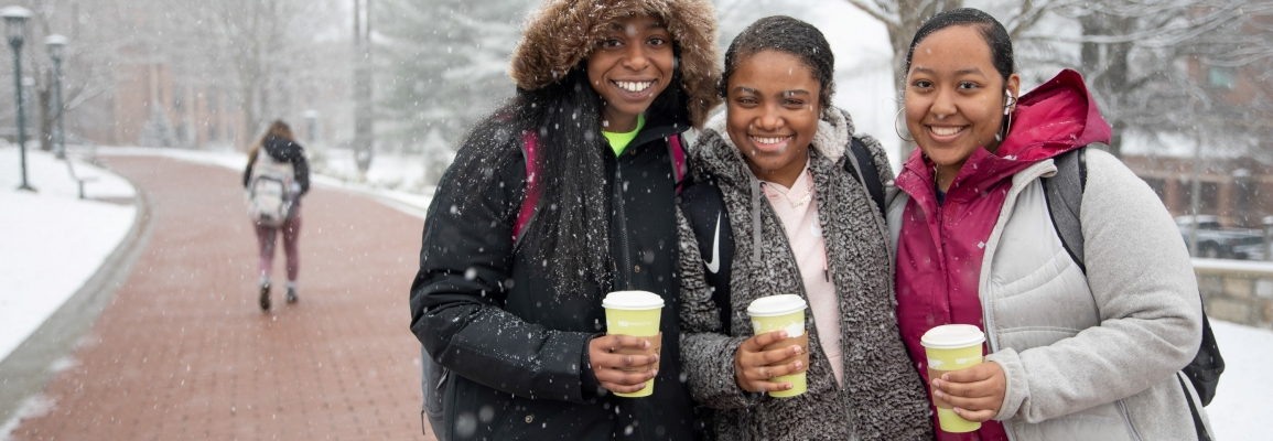 3 students walking on campus while it is snowing 